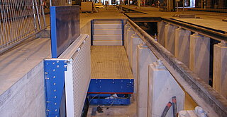 Lifting platforms for lateral working pits Left lateral pit opened: pit cover is folded down, stairs-step are formed, railing is extended and is using as fall protection. Via the stairs, the working level below grond level can be reached.