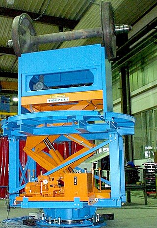 This customer-specific device is used for lifting, rolling and turning wheelsets with and without attachments with fixed track width. Lifting and turning device with wheelset during preliminary acceptance test in the lifted condition. This device will be embedded in a pit on site.